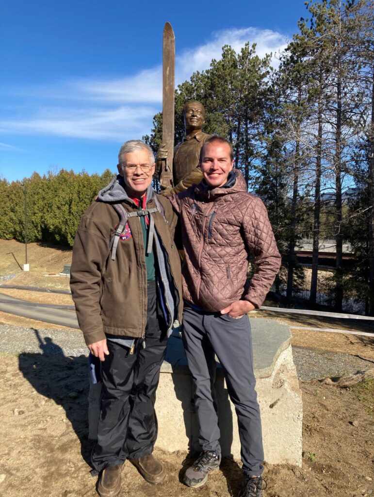 Bill Koch and Billy Demong stand in front of a Statue of Art Devlin at the newly renovated jumps in Lake Placid, NY